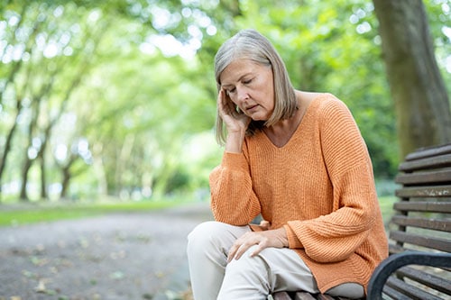 Middle aged woman with low energy sitting on bench in park